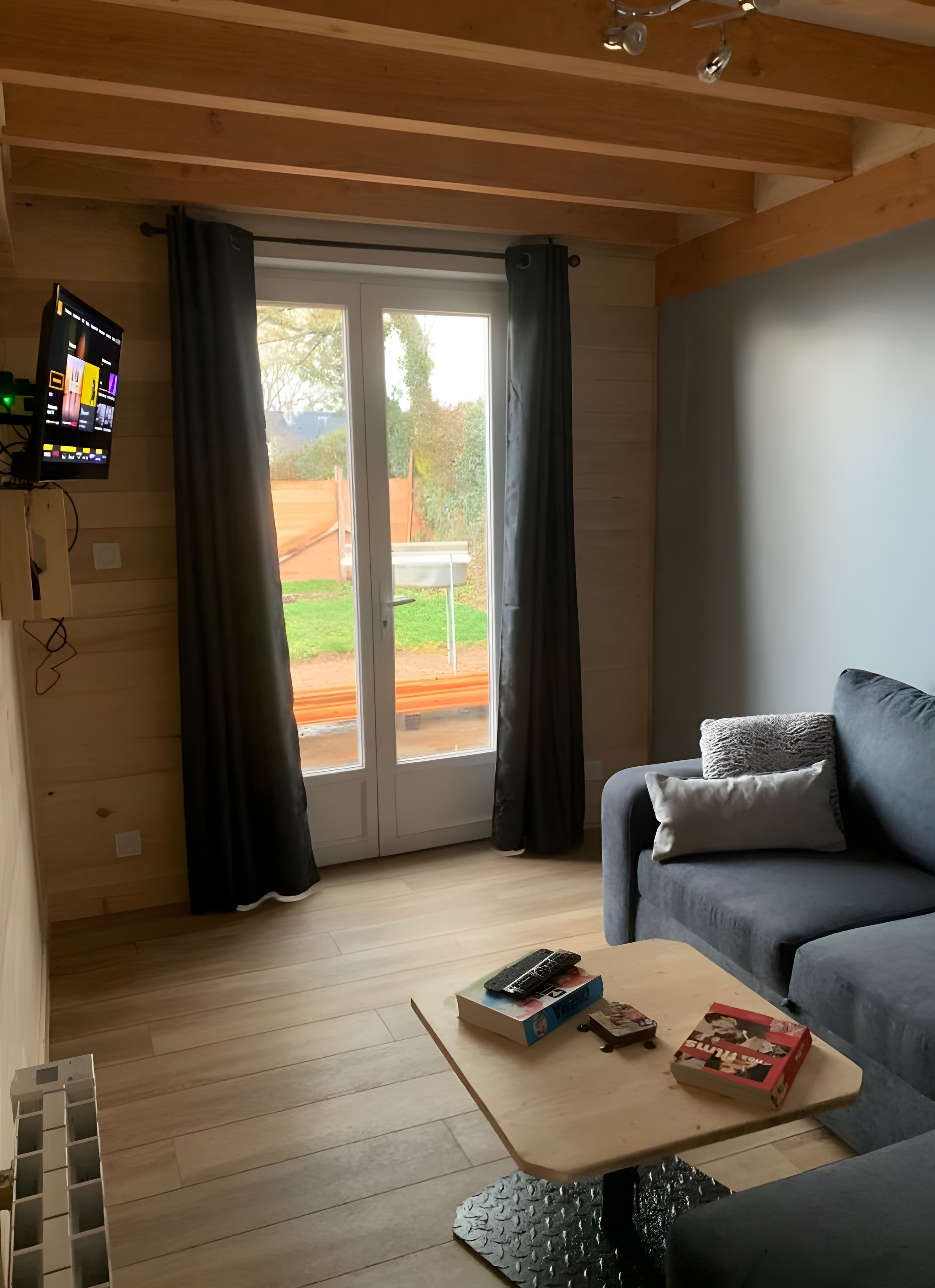 Un salon comprenant un canapé, une table basse, un téléviseur fixé au mur et une porte-fenêtre coulissante donnant sur un espace extérieur.