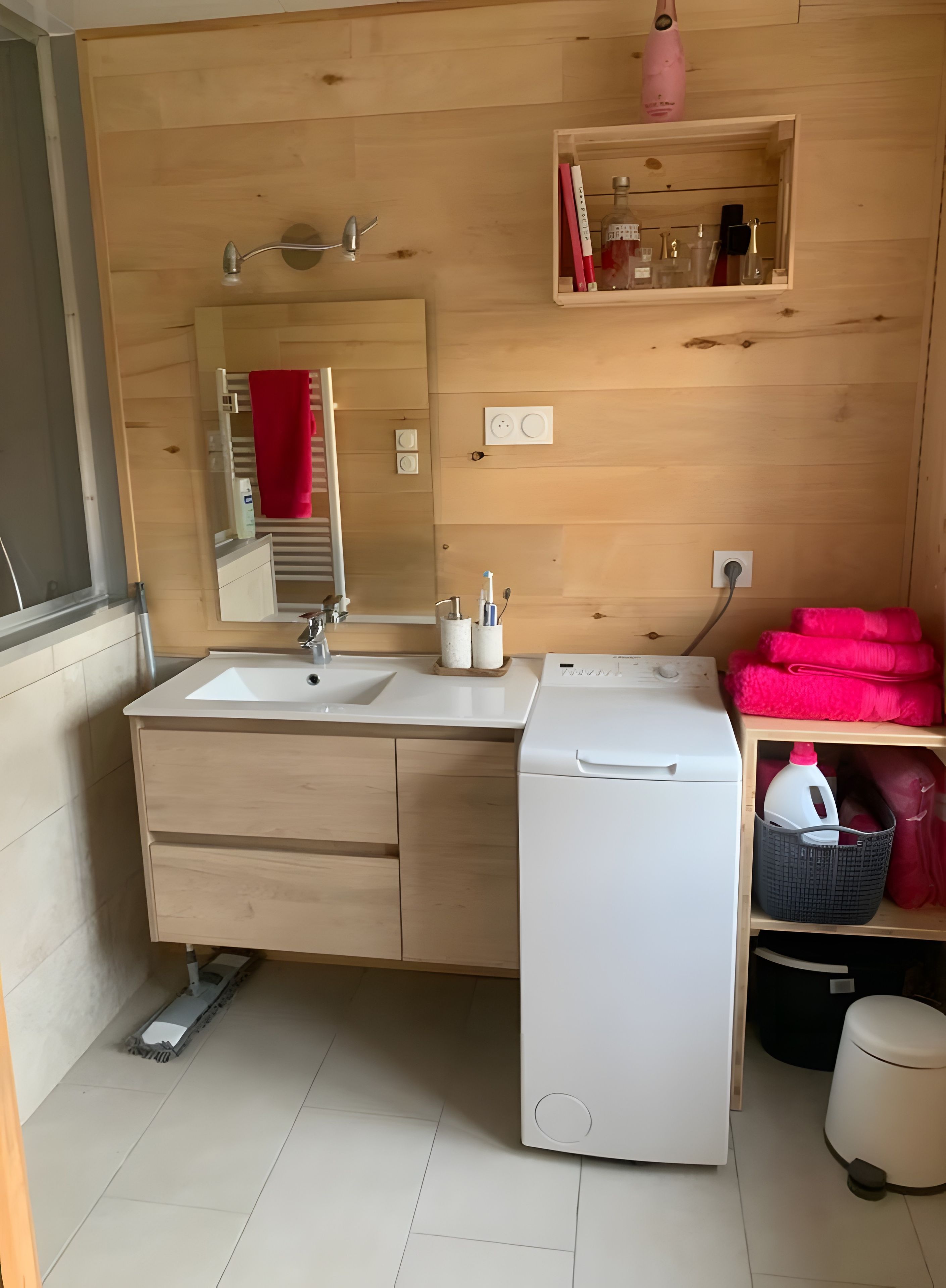Une salle de bain moderne avec deux lavabos, un miroir, un porte-serviettes, une étagère avec des articles de toilette et un lave-linge.