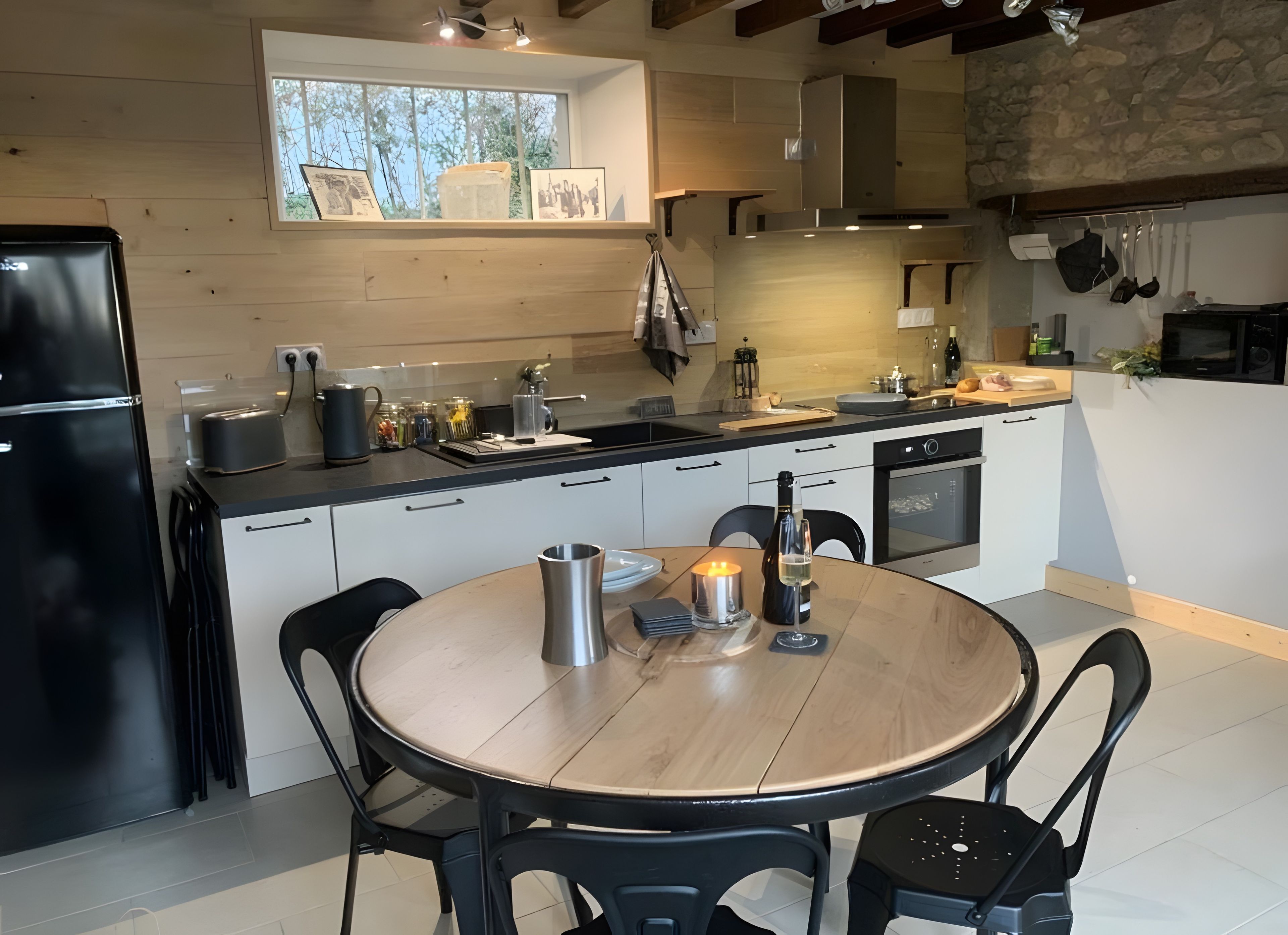 A modern kitchen with a dining area, featuring a refrigerator, stove, sink, and a round table with chairs.