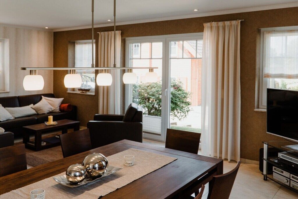 A modern living room with a dining area, a sofa set, a TV, and a large window with curtains.