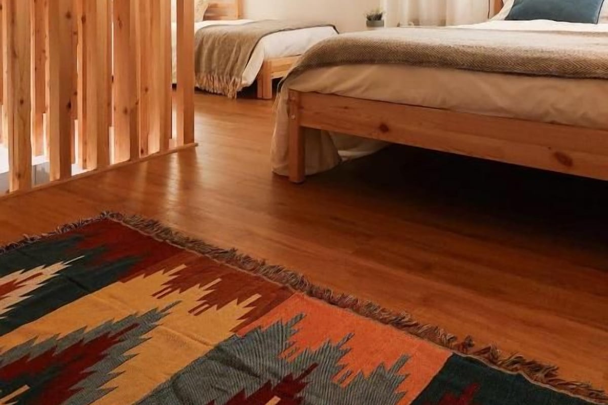Ein Schlafzimmer mit Holzbalkendecke, einem Bett mit blauem Kopfkissen und einem farbenfrohen Teppich.