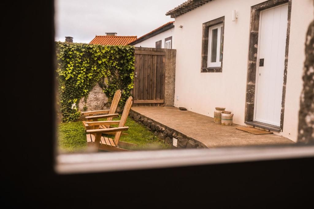 Une terrasse avec une chaise et une table en bois, un bâtiment blanc doté d’une fenêtre et d’une porte, et une clôture en bois.