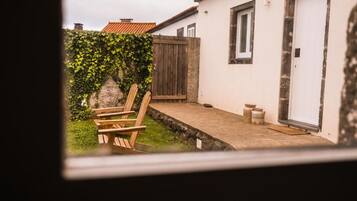 Une terrasse avec une chaise et une table en bois, un bâtiment blanc doté d’une fenêtre et d’une porte, et une clôture en bois.