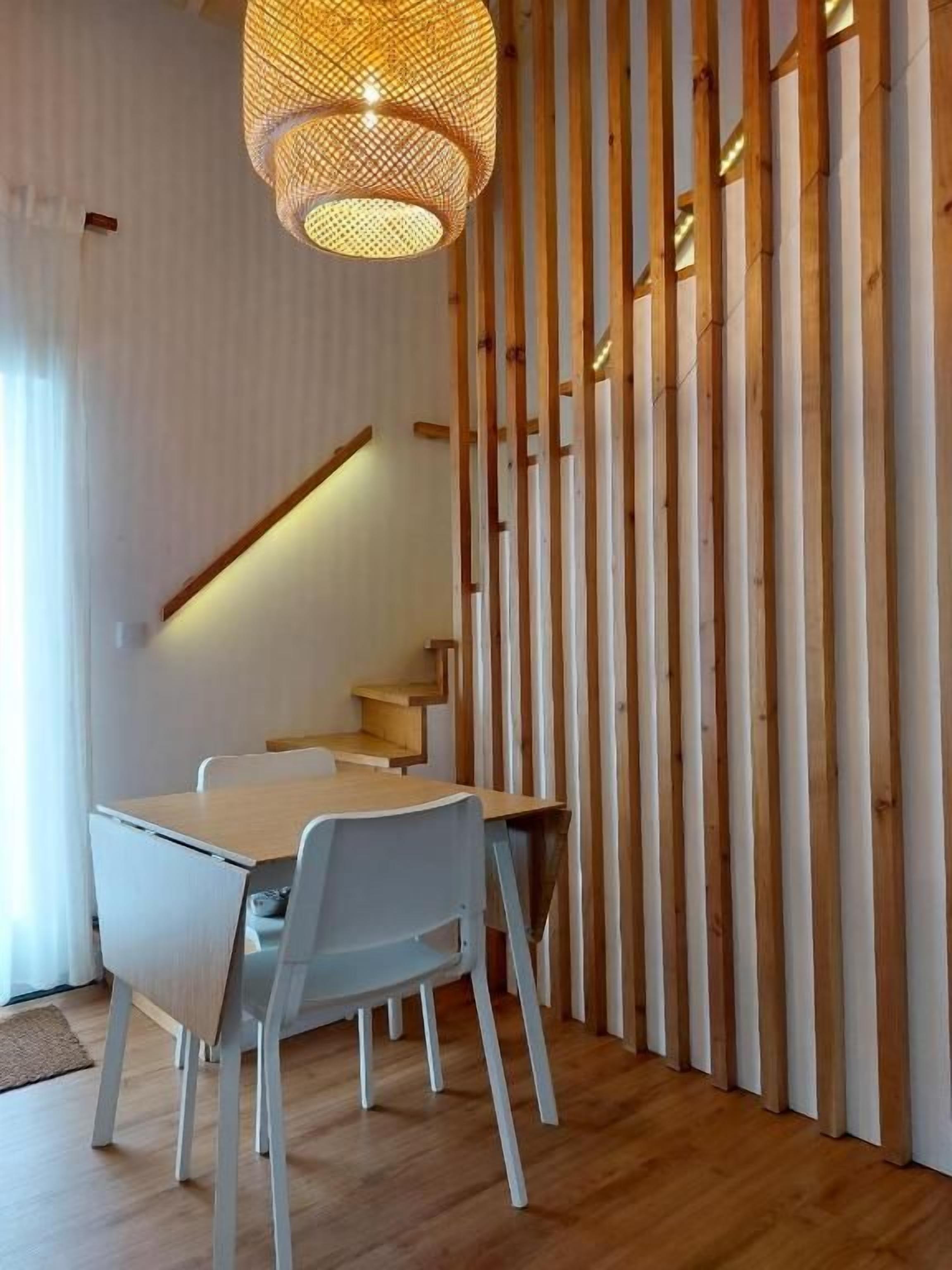 Un comedor con una mesa y sillas, una escalera y una pared con listones de madera verticales.