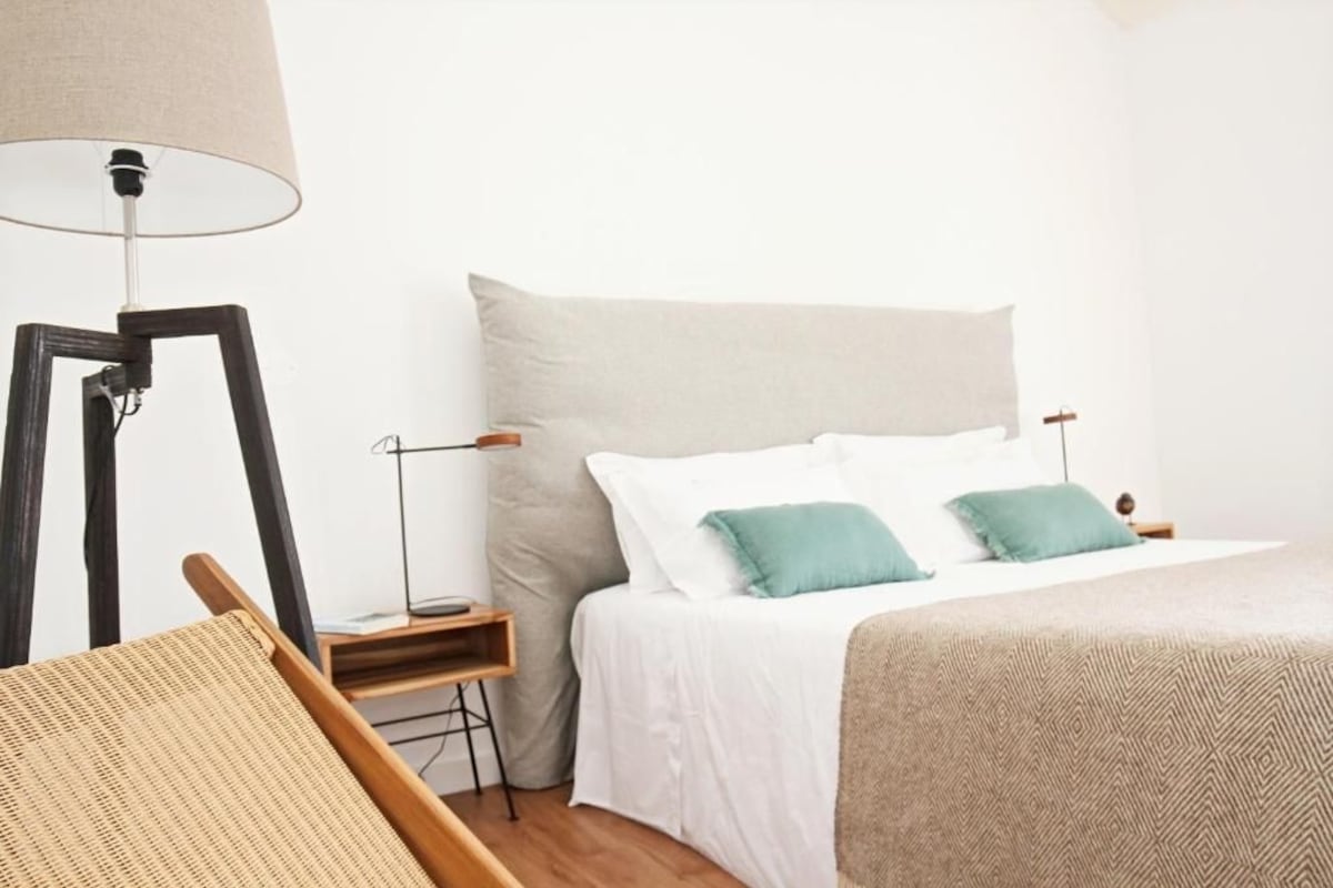 Ein Schlafzimmer mit einem Bett, einem Nachttisch, einer Lampe und einem Sessel.