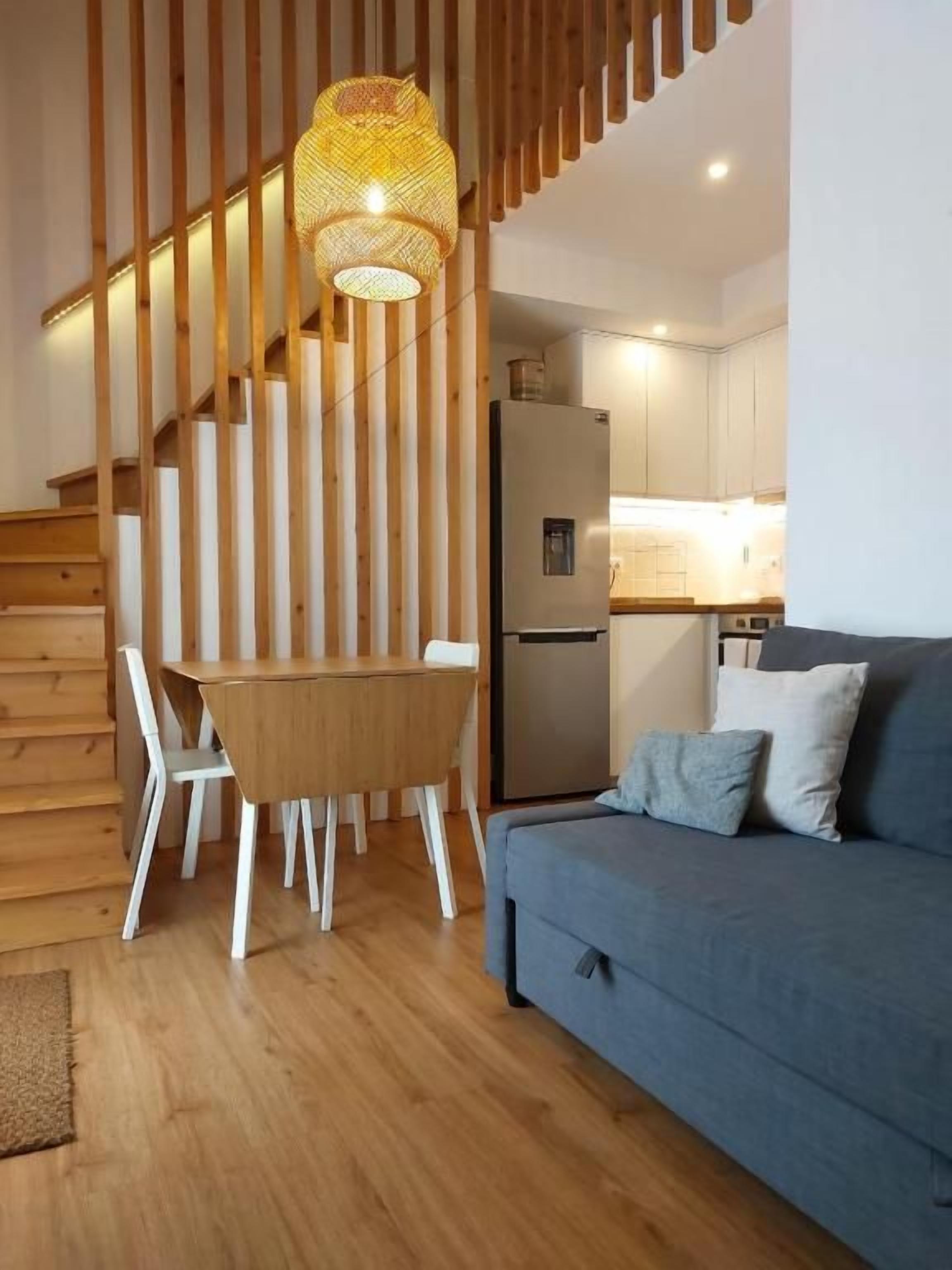 Un interior moderno con una escalera de madera, una zona de comedor con mesa y sillas, y un sofá con cojines.