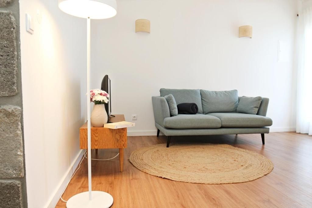 Una sala moderna con un sofá gris, un tapete redondo tejido, una lámpara de pie y una pequeña mesita de madera con un jarrón de flores.