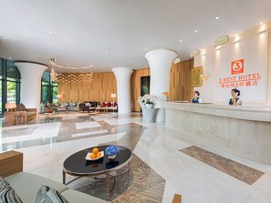 Een hotel receptie met een modern design, inclusief een receptiebalie, een zithoek met banken en een groot raam met uitzicht op het omliggende landschap.