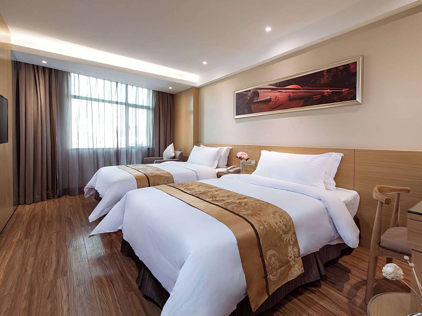 A hotel room with two beds, a large window with curtains, a painting on the wall, and a wooden floor.