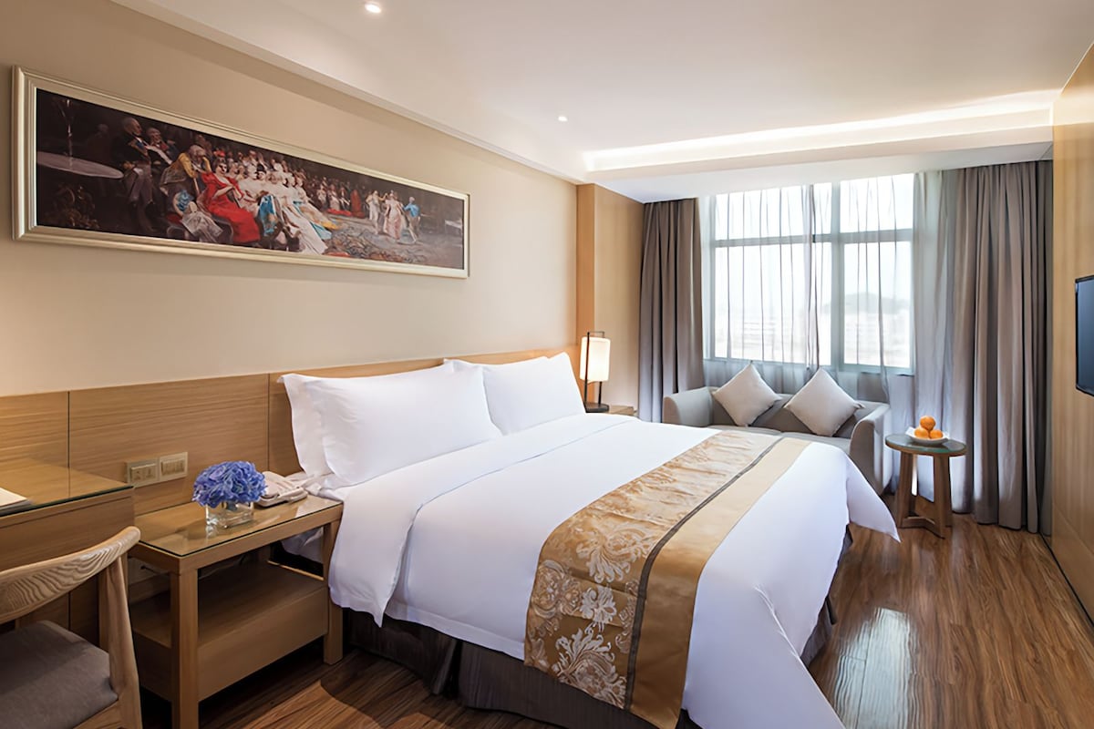 Een hotelkamer met een groot bed, een bureau, een stoel, een televisie en een schilderij aan de muur.