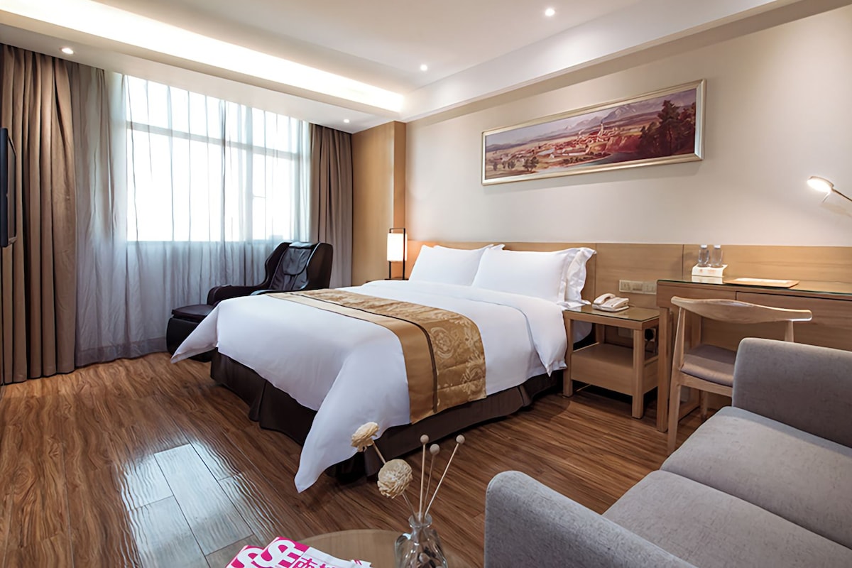 Een hotelkamer met een groot bed, een bureau, een stoel, een massagestoel en een schilderij aan de muur.