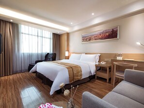 Een hotelkamer met een groot bed, een bureau, een stoel, een massagestoel en een schilderij aan de muur.