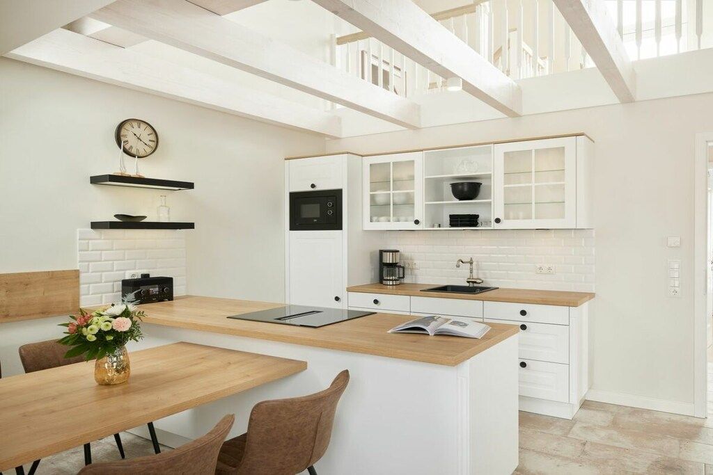 Une cuisine moderne avec des meubles blancs, un plan de travail en bois et un four encastré.