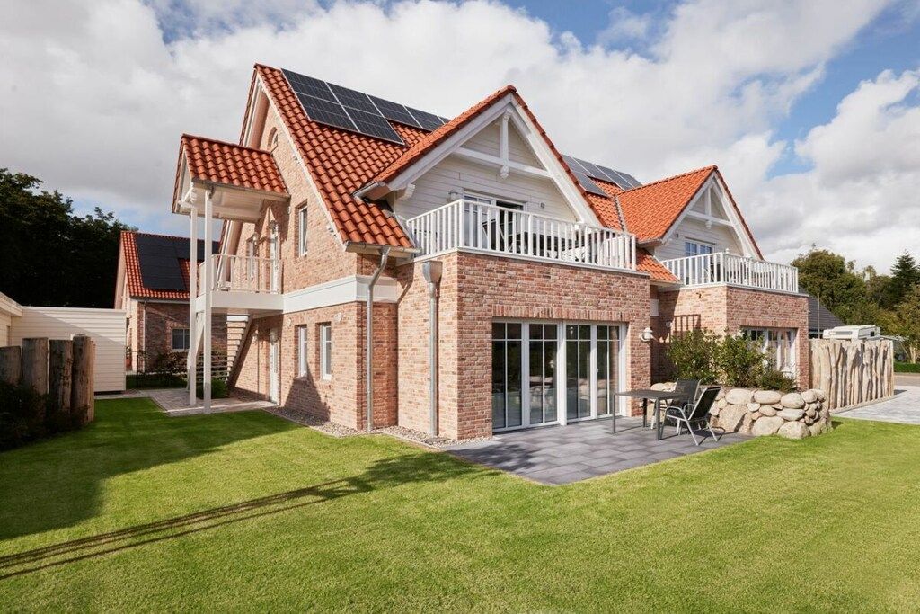 Une maison à deux étages, avec une façade en briques, un toit recouvert de tuiles rouges et des panneaux solaires sur le toit.