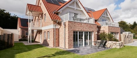 A two-story house with a brick exterior, a red-tiled roof, and solar panels on the roof.