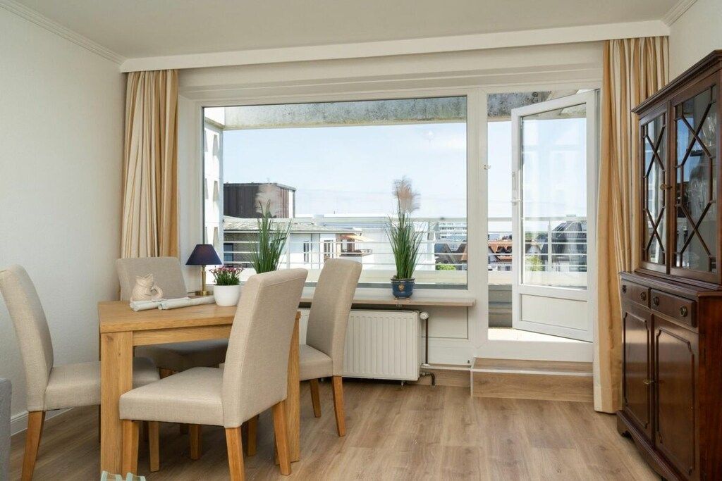 A room with a dining table, chairs, a radiator, a window with curtains, and a cabinet.