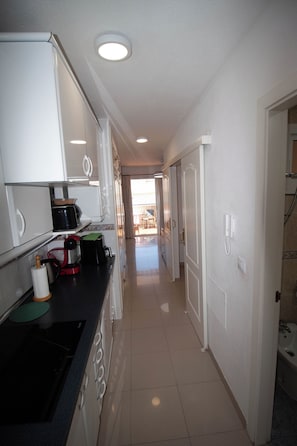 A narrow kitchen with white cabinets, a black countertop, and a tiled floor.