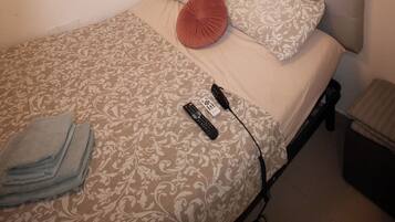 A bedroom with a bed, a bedside table, a window, and a wall-mounted shelf with a plant.