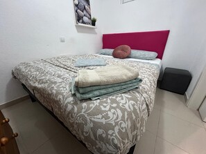 A neatly made bed with patterned bedding and pillows, a small bedside table, and a wall-mounted shelf with a plant. - New Listing (Benalmádena)