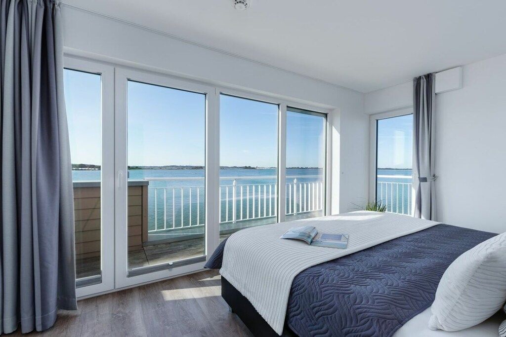 A bedroom with a large bed, a view of the sea, and a balcony with a railing.