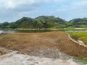 A natural landscape with a body of water, rocky terrain, and hills in the background. - Shakuntalam Lake Village Resort (UDAIPUR)