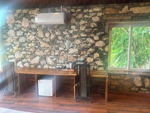 A stone wall, wooden table, and a window with a view of trees. - Shakuntalam Lake Village Resort (UDAIPUR)