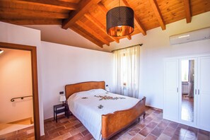 Une chambre avec un plafond en bois, un lit recouvert d’une couvre-lit à motifs floraux, une table de chevet et une fenêtre avec des rideaux.