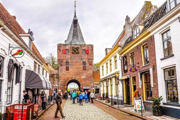 A cobblestone street with a prominent brick tower featuring a clock, flanked by traditional buildings with shops and outdoor seating. - Comfortable Stay Near Walibi Holland (Biddinghuizen)