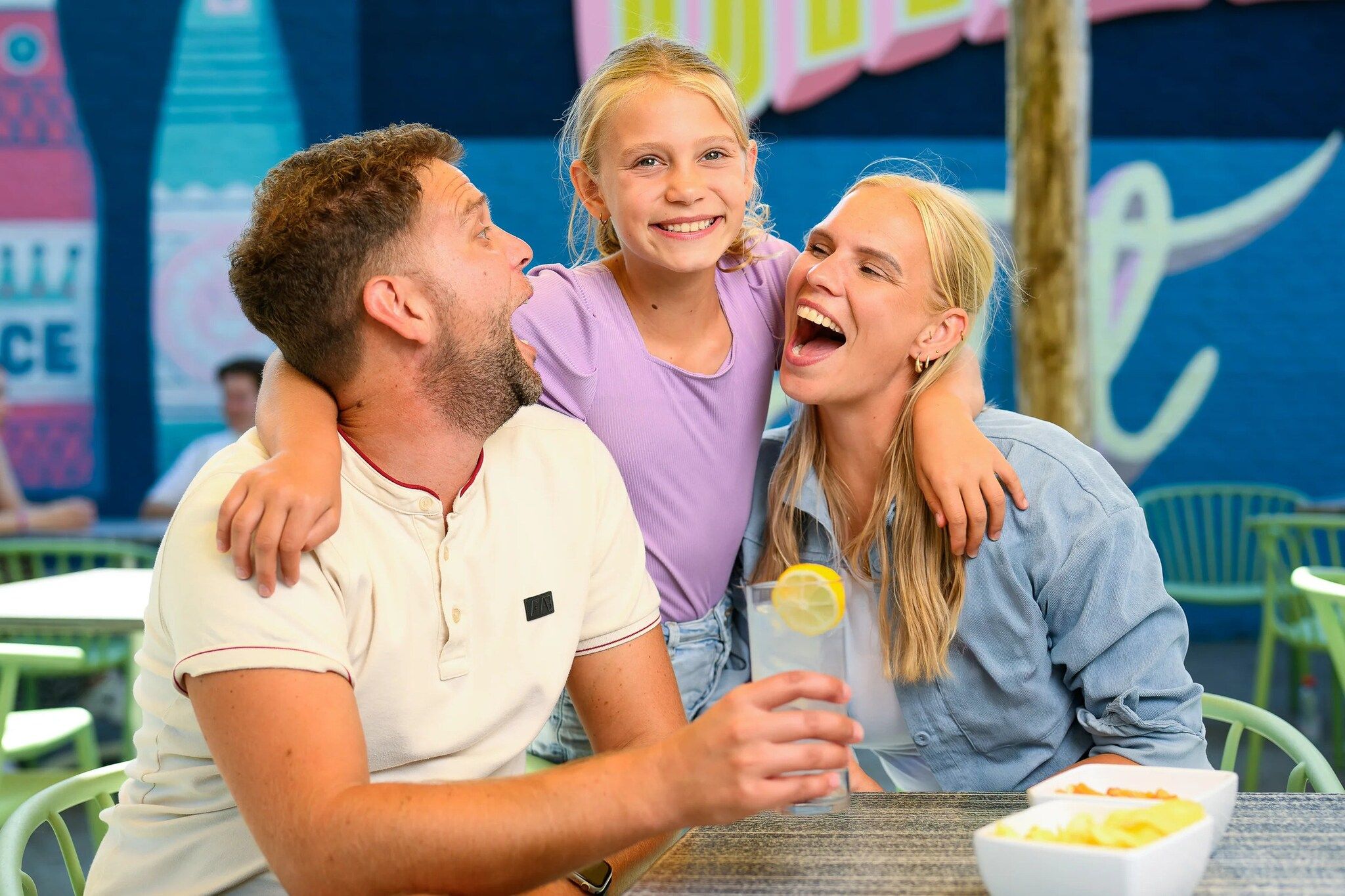 En familie på tre ved et bord med en skål mad og en drik.