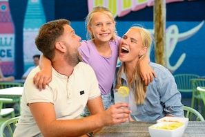 Una familia de tres personas sentada a una mesa, con un plato de comida y una bebida.