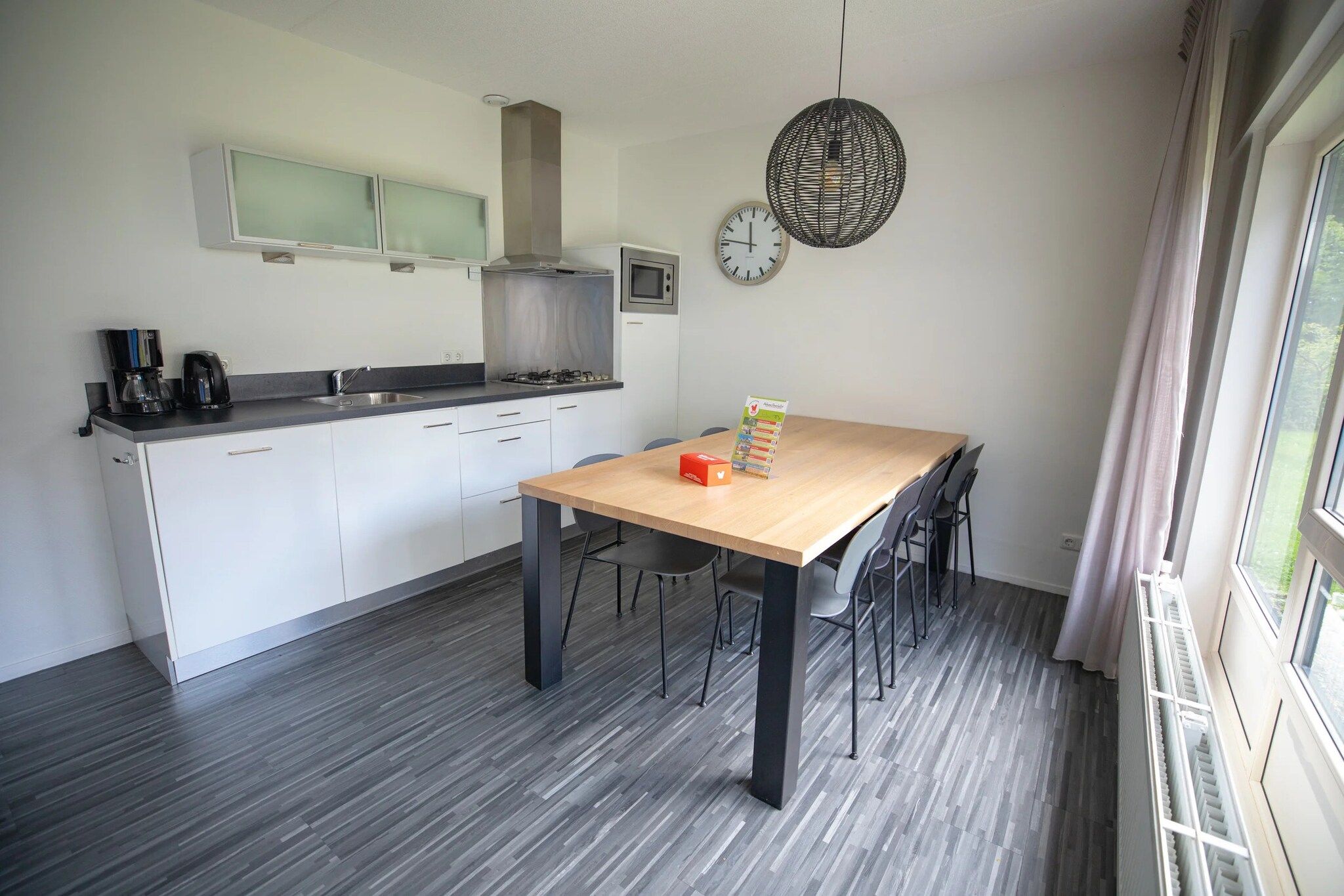 A modern kitchen with a dining area, a clock, and a window with curtains.