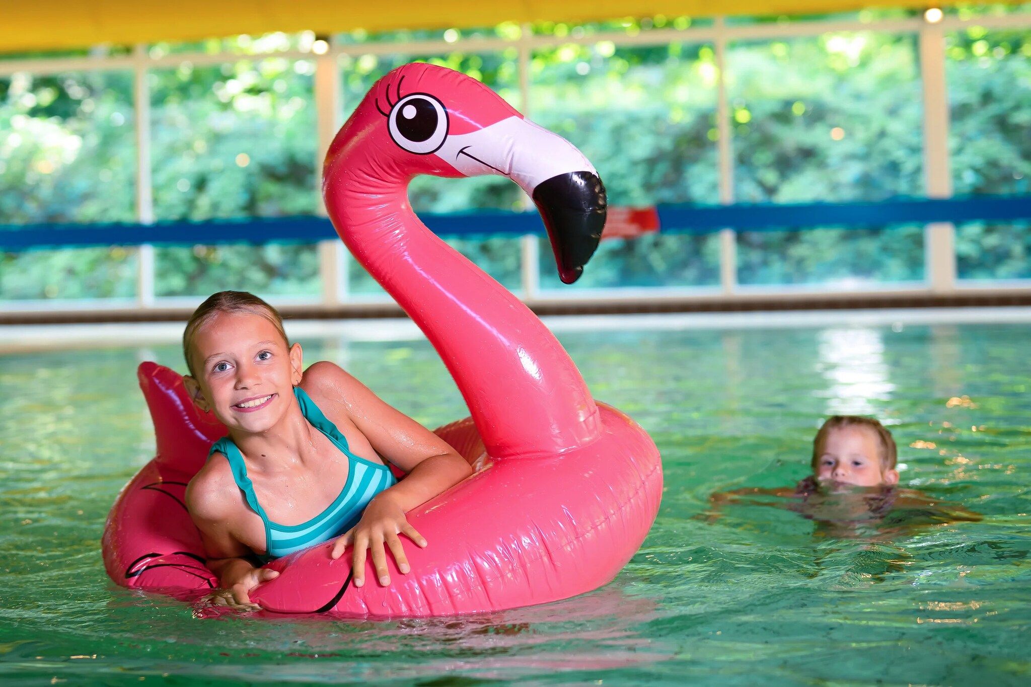 A person in a swimming pool using a pink flamingo float.