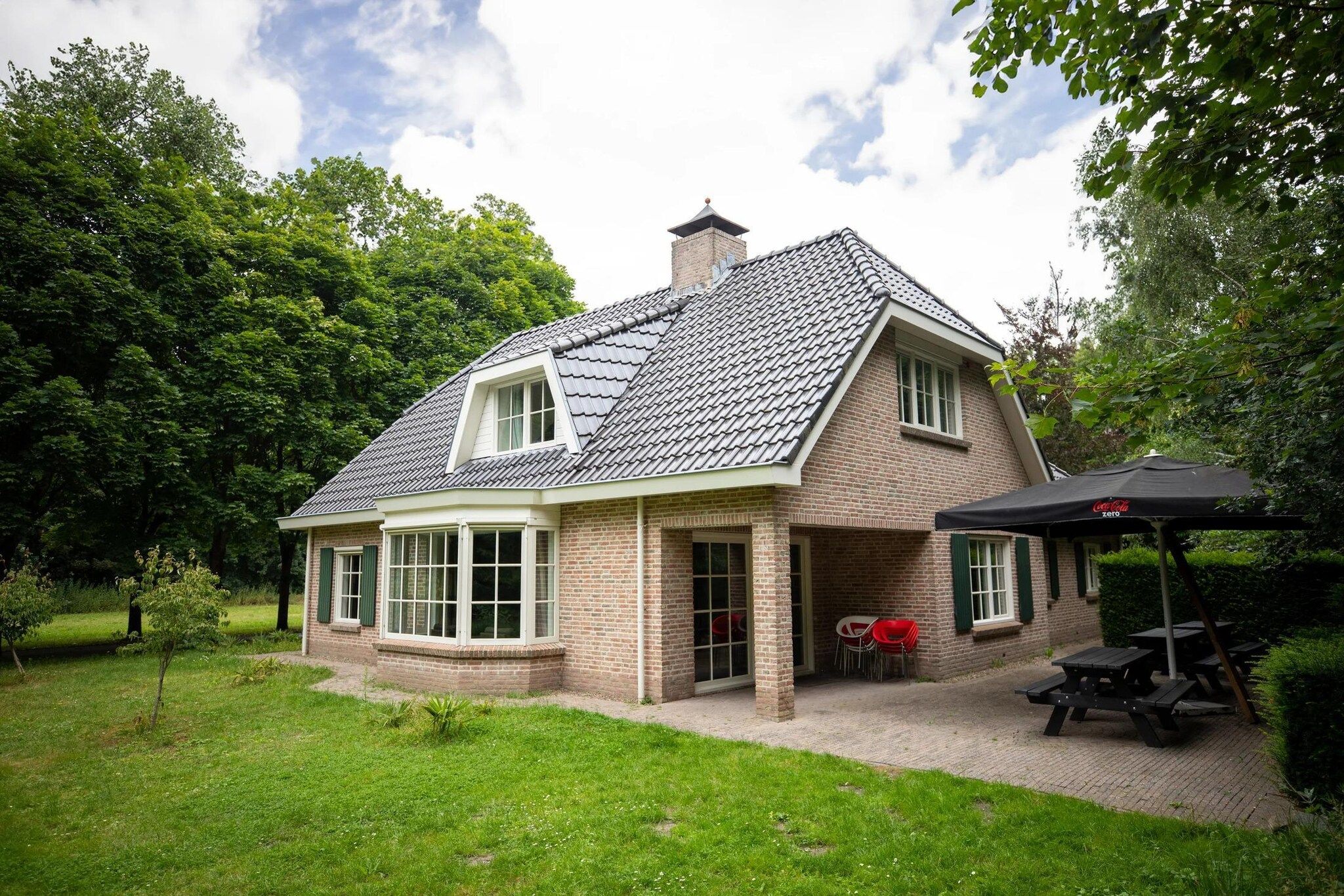 Et hus med murstensfacade, skråt tag og en terrasse med udendørs møbler.