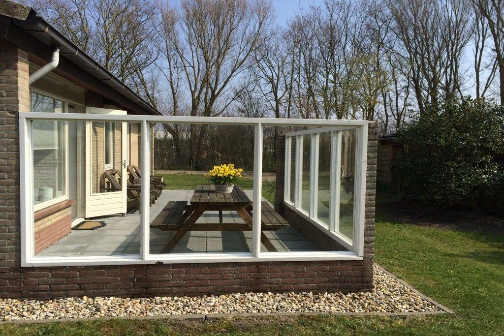 A house with a conservatory featuring a glass enclosure, a wooden table with chairs, and a flower pot.