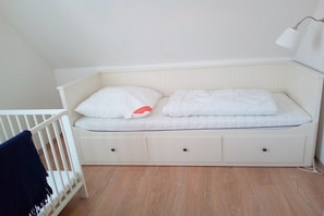 Ein weißes Bett mit zwei Kissen, ein weißer Nachttisch mit Schubladen und eine Wandleuchte.