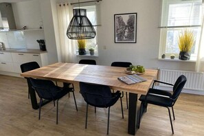 Une cuisine moderne avec une table à manger en bois, des chaises noires et un luminaire suspendu.