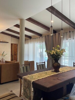 Een eethoek met een lange tafel, stoelen, een vaas met bloemen en uitzicht op het omliggende landschap door grote ramen.