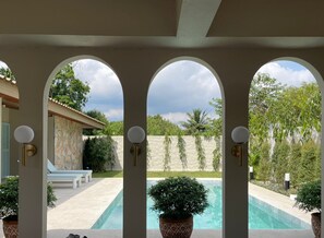 Área de piscina com muro de pedra, um banco e plantas em vasos.