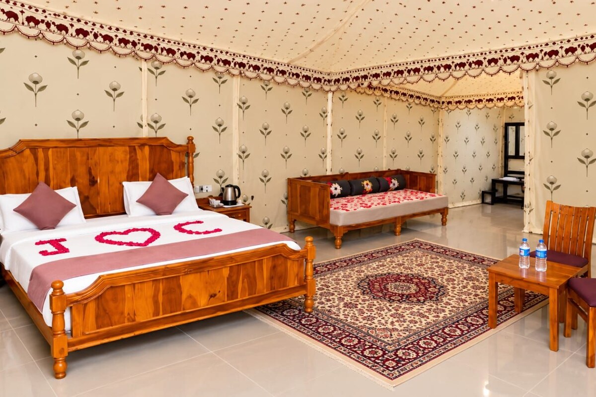 A hotel room with a wooden bed, a sofa, a dining table with chairs, and a patterned rug.