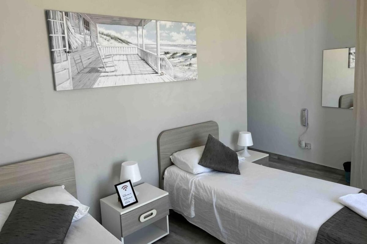 Ein Hotelzimmer mit zwei Betten, einem Strandbild, einem Nachttisch mit Lampe und einem Spiegel.