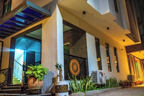 Entrada de hotel con una escalera, plantas en macetas y un muro decorativo.