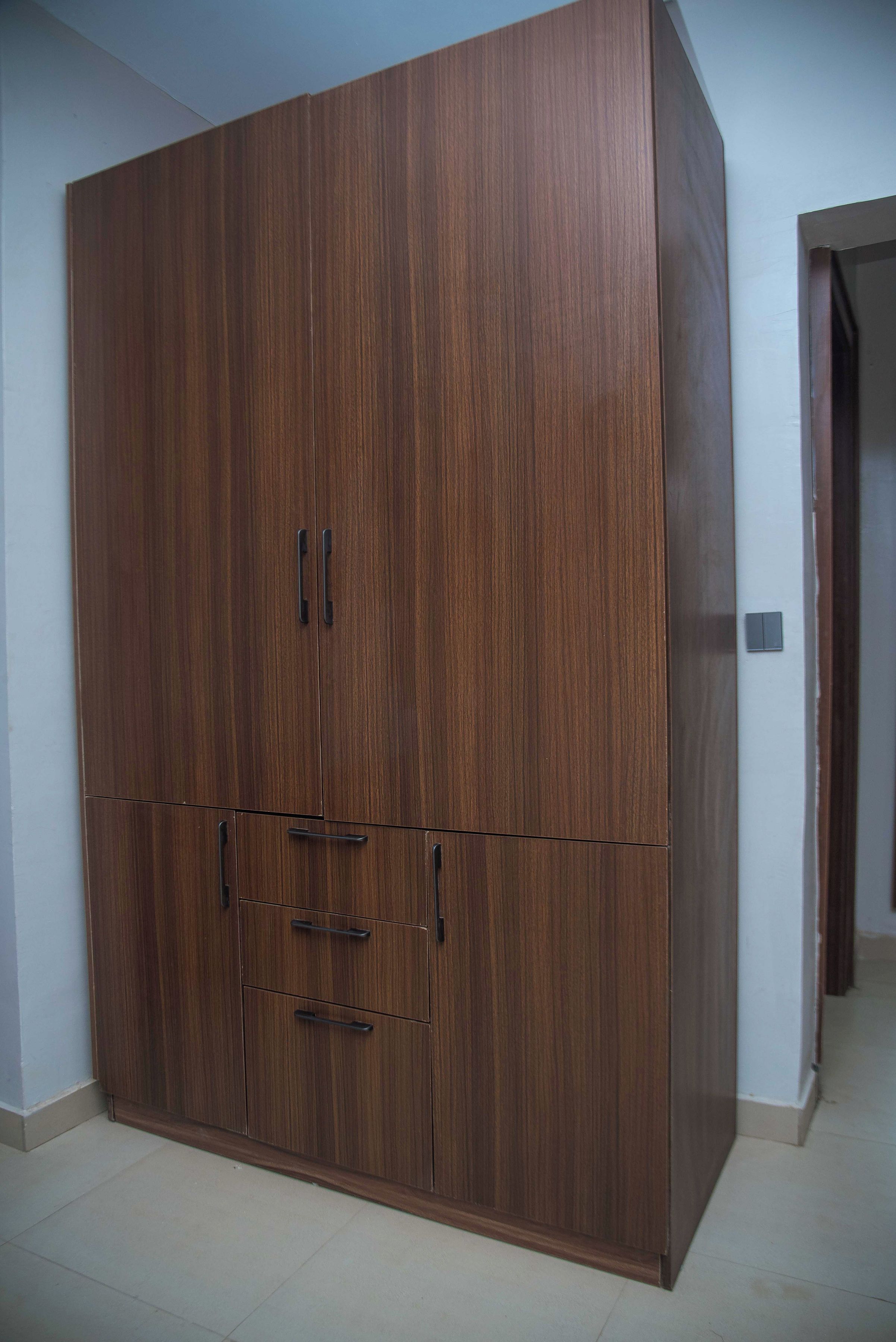 A large wardrobe with multiple doors and drawers, a light-colored tiled floor, and a plain wall.