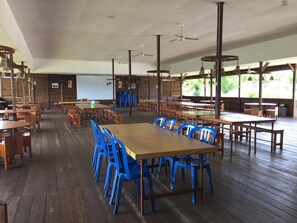 A spacious indoor area with multiple wooden tables and blue plastic chairs, featuring ceiling fans and natural light from large windows. - Pelangi Lake Resort and Hotel Belitung (Tanjung Pandan)