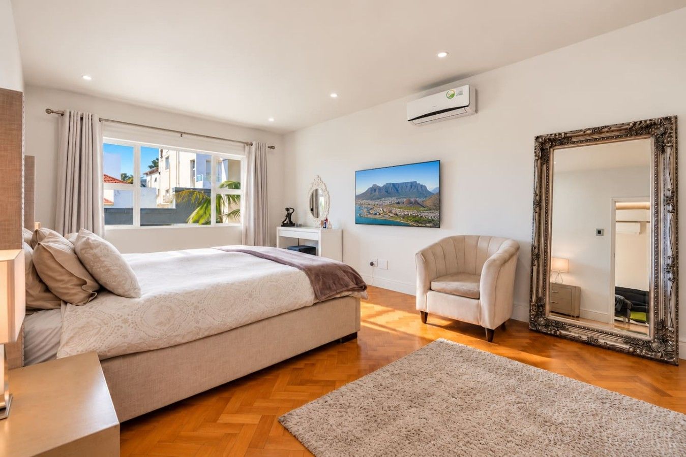 Une chambre à coucher avec un lit, une chaise, un grand miroir et un tableau accroché au mur.
