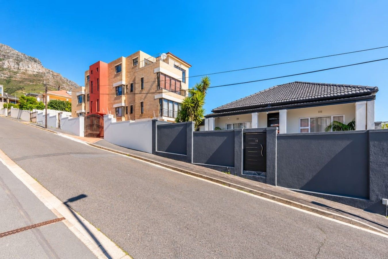 A residential street with modern houses, a gated entrance, and a clear sky.