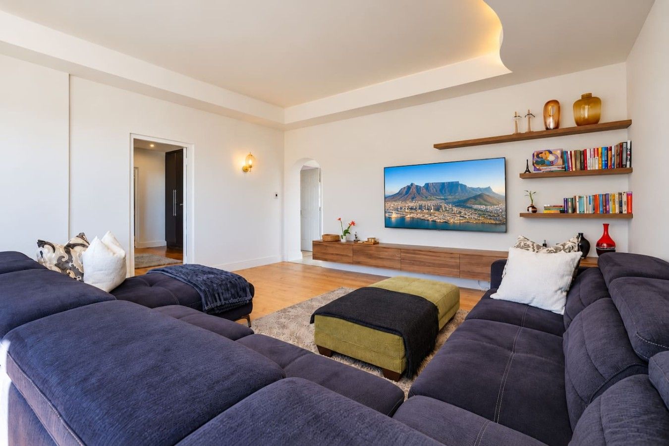 A modern living room with dark sofas, a wooden coffee table, and a large landscape painting on the wall.
