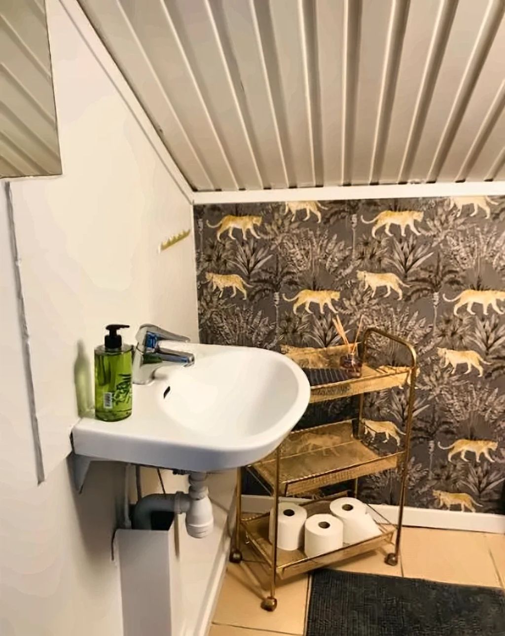 A bathroom with a white sink, a gold vanity, and a patterned wallpaper.