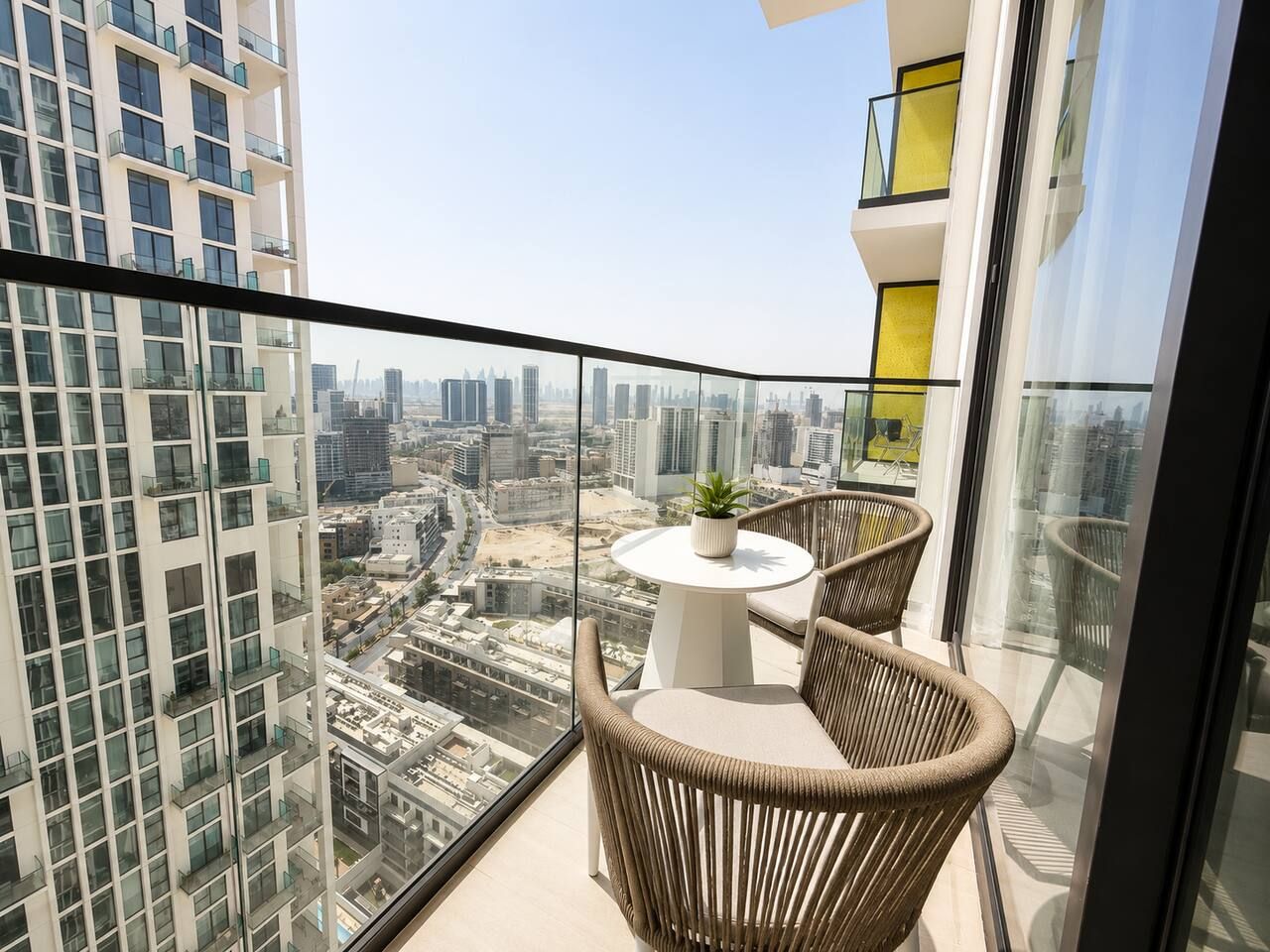 A balcony with a glass railing, a round table with a potted plant, and wicker chairs.