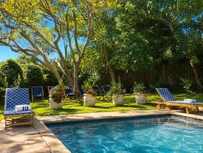 Un patio trasero con piscina, sillas de descanso y plantas en macetas.