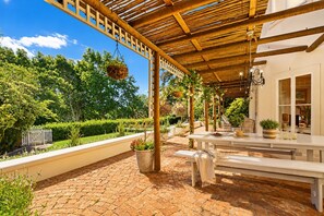 Un patio exterior con pérgola, asientos y plantas en macetas.
